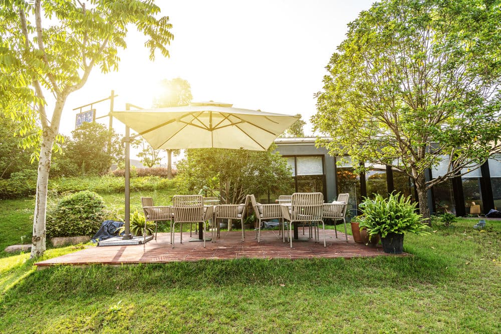 Cozy outdoor patio with umbrella and seating, surrounded by greenery and sunlight.